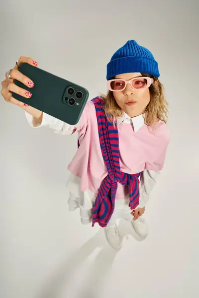 Pretty young woman in a stylish outfit poses and takes a selfie in a contemporary studio. — Stock Photo