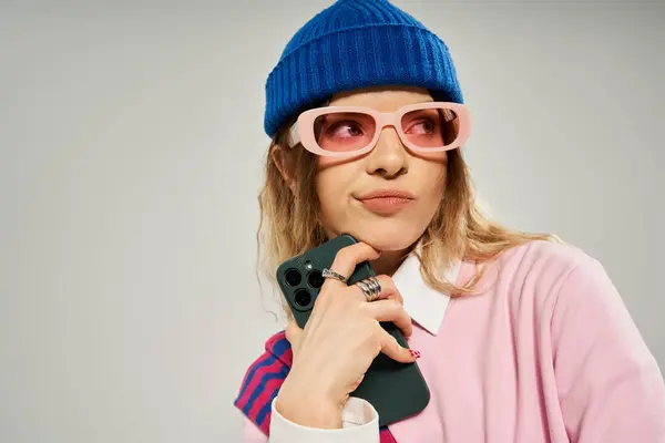 A pretty woman in a trendy outfit holds her phone while striking a playful pose in a studio. — Stock Photo
