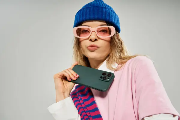 A pretty young woman showcases her fashionable look while holding a smartphone in a studio. — Stock Photo