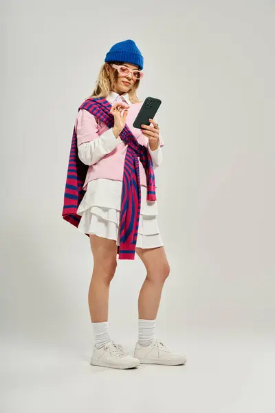 Pretty young woman showcases trendy fashion while happily engaging with her phone in bright studio. — Stock Photo