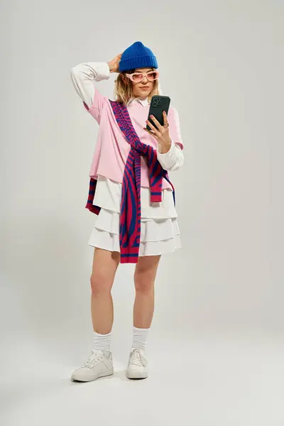 Eine junge Frau zeigt ihr trendiges Outfit und ihre leuchtend blaue Mütze, während sie ein Selfie im Studio macht. — Stockfoto