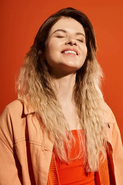 Young woman radiates joy in a trendy outfit, captivating with style on a warm orange background. — Stock Photo