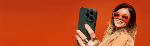 Pretty young woman wearing stylish outfit smiles while taking a selfie with her phone. — Stock Photo