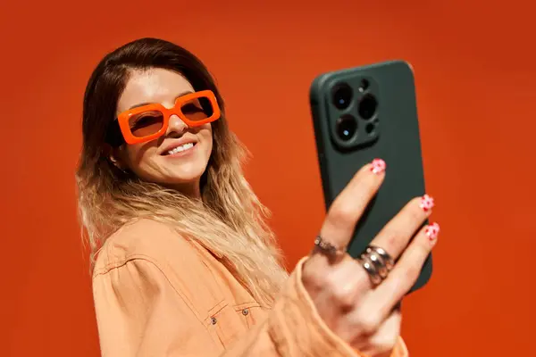 Stylish young woman happily takes a selfie while wearing vibrant glasses and a trendy outfit. — Stock Photo