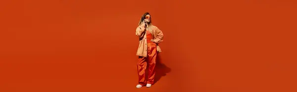 Mujer joven brillantemente vestida con confianza posa sobre un fondo naranja, irradiando estilo y energía. - foto de stock