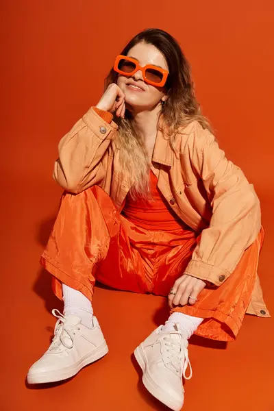 A young woman with a cheerful expression showcases her fashionable orange ensemble while sitting. — Stock Photo