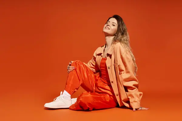 Une jeune femme modèle sa tenue colorée sur un fond orange vif. — Photo de stock