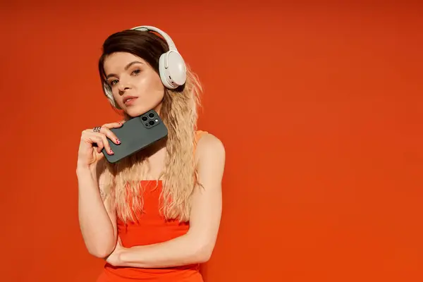 A young woman poses confidently in a vibrant outfit, holding a phone while wearing headphones. — Stock Photo