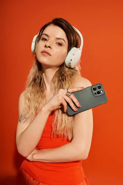 A young woman radiates charm wearing an eye-catching outfit against an orange backdrop. — Stock Photo