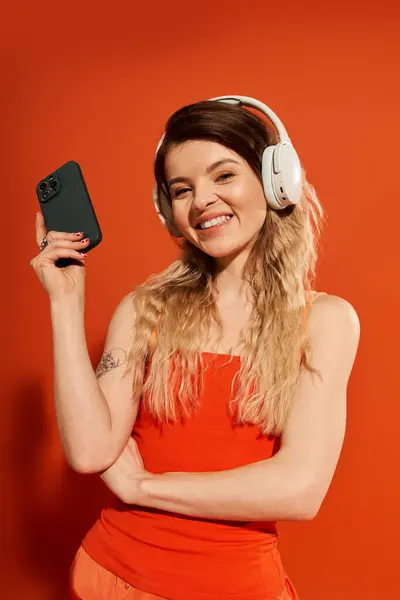 A pretty young woman smiles, wearing headphones and holding a smartphone, embodying joy and style. — Stock Photo