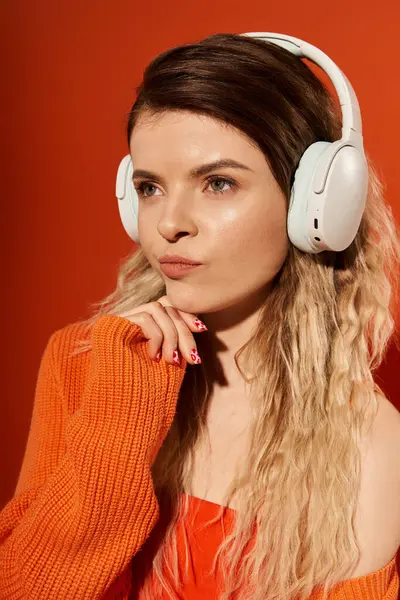 A young woman in an orange outfit listens to music with headphones, deep in thought. — Stock Photo