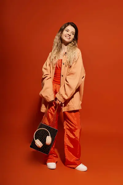Jolie jeune femme rayonne de joie dans sa superbe tenue orange sur un fond vibrant. — Photo de stock