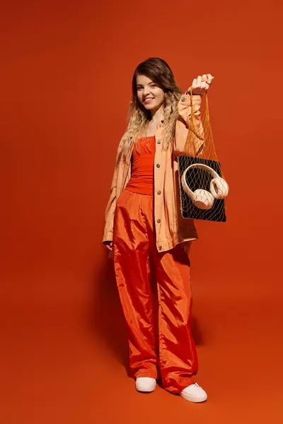 A young woman radiates happiness while holding a stylish outfit, set against an orange backdrop. — Stock Photo