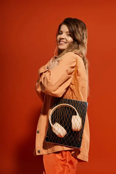 A young woman flaunts her stylish outfit and handbag against a vibrant orange backdrop. — Stock Photo