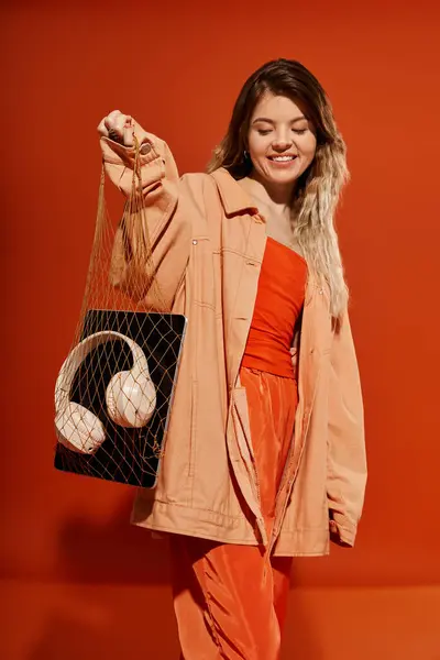 A stylish young woman showcases her fashionable outfit while playfully holding a chic bag. — Stock Photo