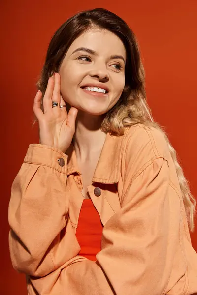 A pretty young woman smiles brightly, showcasing her vibrant outfit on a bold orange background. — Stock Photo