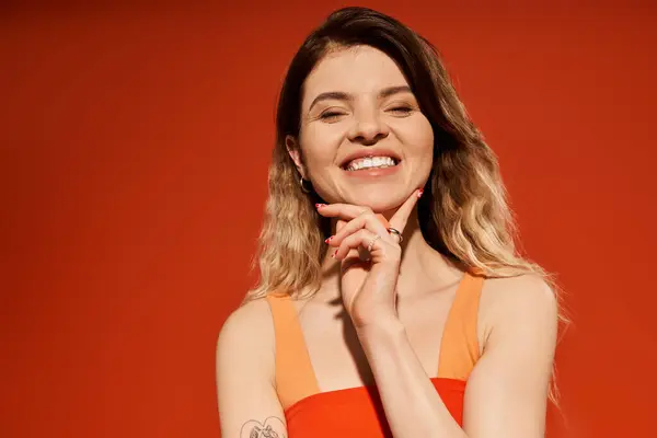 Young woman smiles brightly while posing in a stylish outfit on an orange background. — Stock Photo