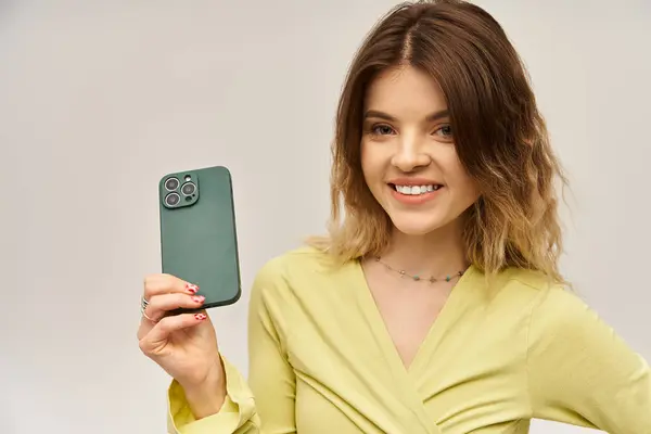 A beautiful young woman smiles confidently in a fashionable outfit against a grey backdrop. — Stock Photo