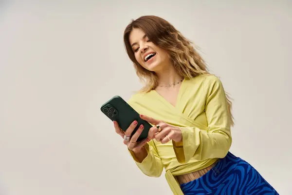 A young woman smiles at her smartphone, showing off her stylish outfit. — Stock Photo