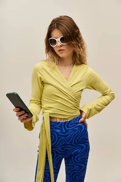 A beautiful young woman stands confidently, dressed in a vibrant outfit while holding her phone. — Stock Photo