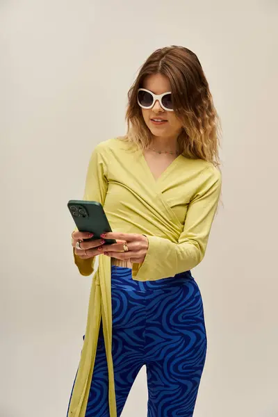 A beautiful young woman checks her phone while dressed in a trendy outfit, exuding confidence. — Stock Photo