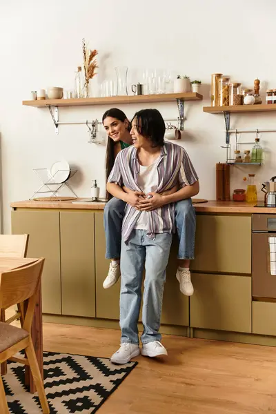 Couple laughs warmly, with one playfully perched on the others back in a chic kitchen. — Stock Photo