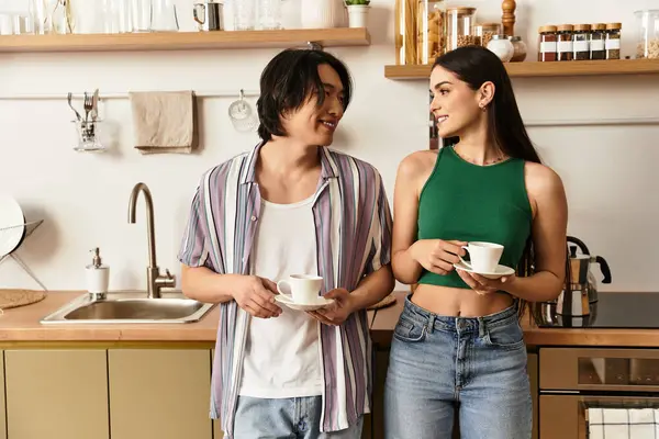 Paar in heller Küche tauscht Lächeln aus, während es Kaffeetassen in der Hand hält und Liebe und Freude ausstrahlt. — Stockfoto
