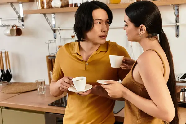 Couple enjoys warm cups of coffee together while sharing smiles and laughter in their kitchen. — Stock Photo