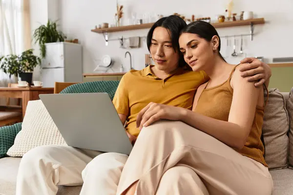 A couple sits comfortably on a sofa, sharing affection while looking at a laptop screen. — Stock Photo