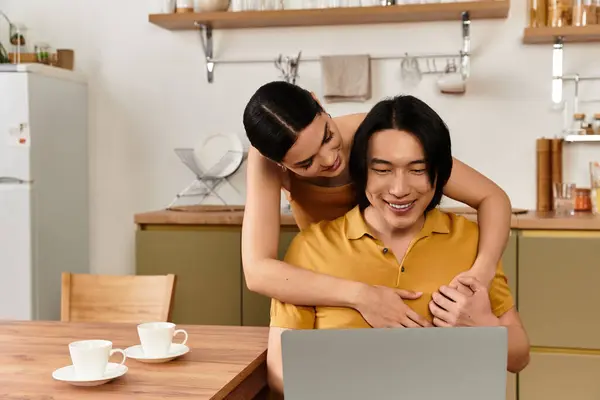 A loving couple shares laughter and affection in their cozy kitchen as they connect online. — Stock Photo