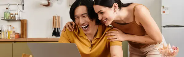 Loving partners share joy and affection as they bond over a laptop in their inviting kitchen space. — Stock Photo