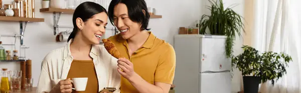 Couple shares a sweet moment at home, smiling over coffee and a croissant. — Stock Photo