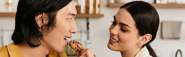 Um casal sorri enquanto se alimentam uns aos outros biscoitos em sua cozinha acolhedora. — Fotografia de Stock