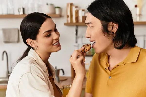 Loving duo enjoy a playful moment together, sharing a cookie and smiles in a warm home setting. — Stock Photo