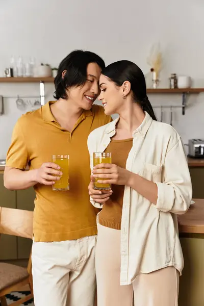 A couple shares a joyful moment at home, holding glasses of drinks and smiling at each other. — Stock Photo