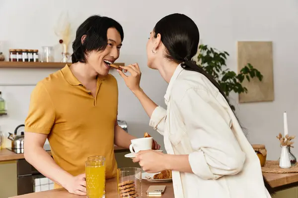 Um casal desfruta de um momento de coração leve enquanto compartilha um lanche e bebidas em sua mesa de cozinha. — Fotografia de Stock
