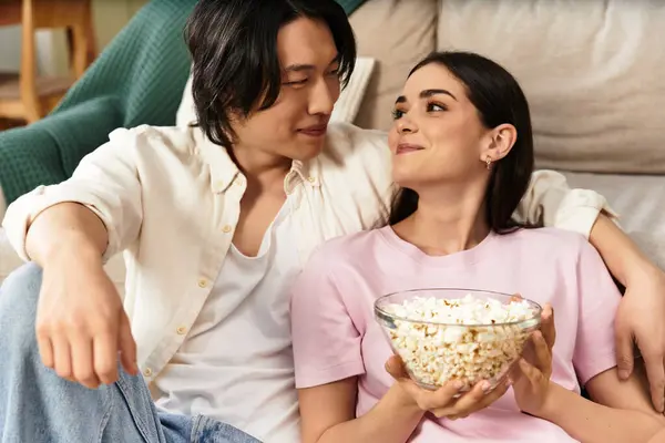 Loving couple sharing a bowl of popcorn while relaxing on their couch in a warm atmosphere. — Stock Photo