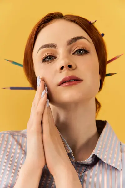 A young woman with striking features has colored pencils playfully arranged in her hair. — Stock Photo