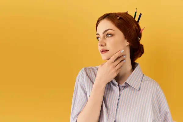 A beautiful young woman with orange hair contemplates creativity against a bright yellow backdrop. — Stock Photo