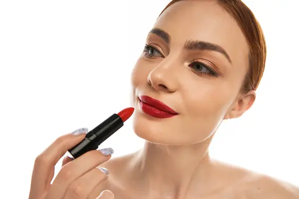 Una hermosa joven mujer realza sus labios con lápiz labial rojo audaz mientras muestra su sonrisa agraciada - foto de stock