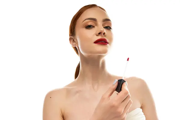 Una mujer joven aplica lápiz labial rojo audaz, irradiando confianza sobre un fondo limpio. - foto de stock