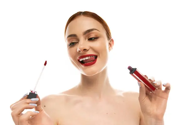 Una joven mujer felizmente aplica lápiz labial rojo audaz, mostrando su belleza y confianza. - foto de stock