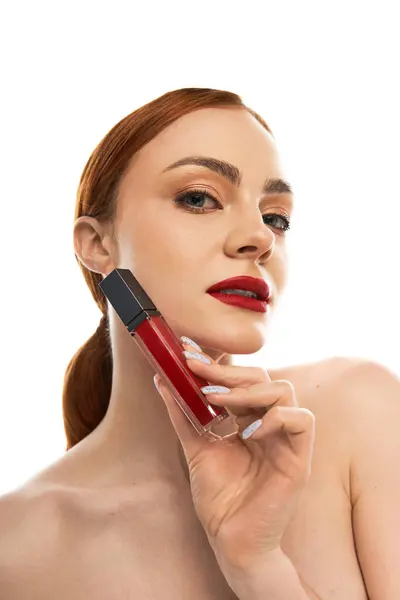 Young woman holding a vibrant red lip product while highlighting her natural beauty with confidence. — Stock Photo