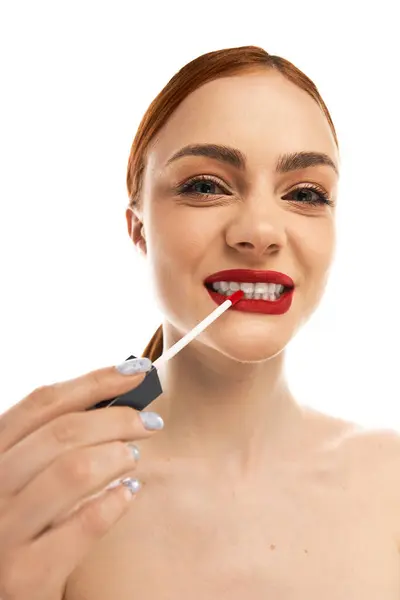 Giovane donna con i capelli rossi migliora la sua bellezza applicando rossetto audace mentre sorride ampiamente. — Foto stock
