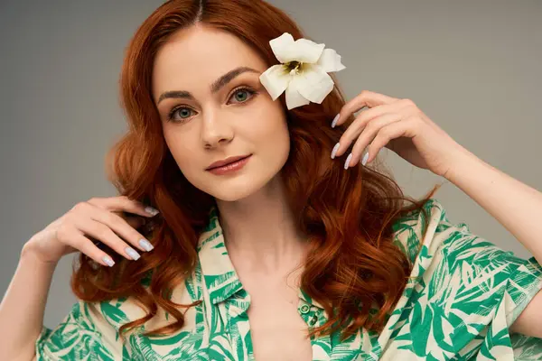 Eine atemberaubende junge Frau mit wallenden roten Haaren und einer weißen Blume passt ihre Haare an und versprüht Charme. — Stockfoto