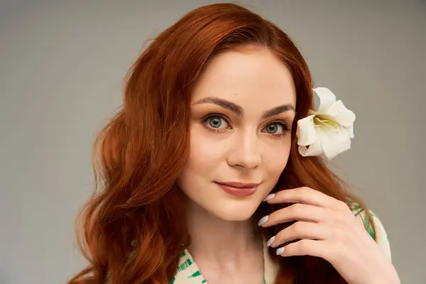 Une jeune femme aux cheveux roux touche doucement son visage, mettant en valeur une fleur délicate. — Photo de stock