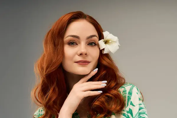 Eine selbstbewusste Frau mit wallenden roten Haaren berührt ihr Gesicht sanft, eine weiße Blume im Haar. — Stockfoto