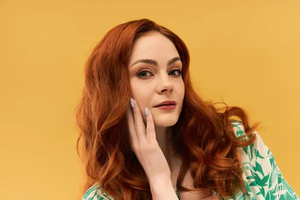 A beautiful young woman with flowing red hair gently touches her face, smiling confidently. — Stock Photo