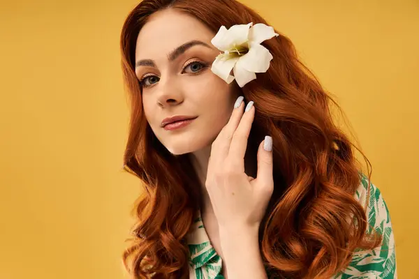 Eine junge Frau berührt sanft ihr Haar, während sie in ihren langen, roten Locken eine wunderschöne Blume zur Schau stellt. — Stockfoto