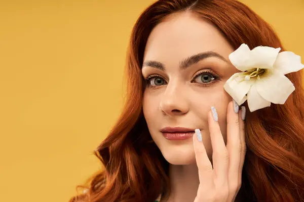 Radiant woman enhances her beauty with a delicate flower while caressing her cheek. — Stock Photo